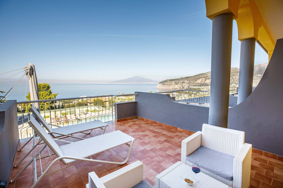 Ein Balkon mit Blick auf das Meer und ein Berg, ausgestattet mit weißen Stühlen und einem Tisch.