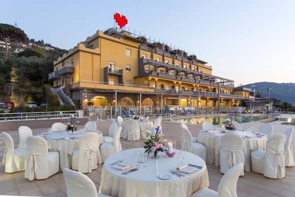 Un hotel con zonas de comedor al aire libre, varios balcones y una piscina.
