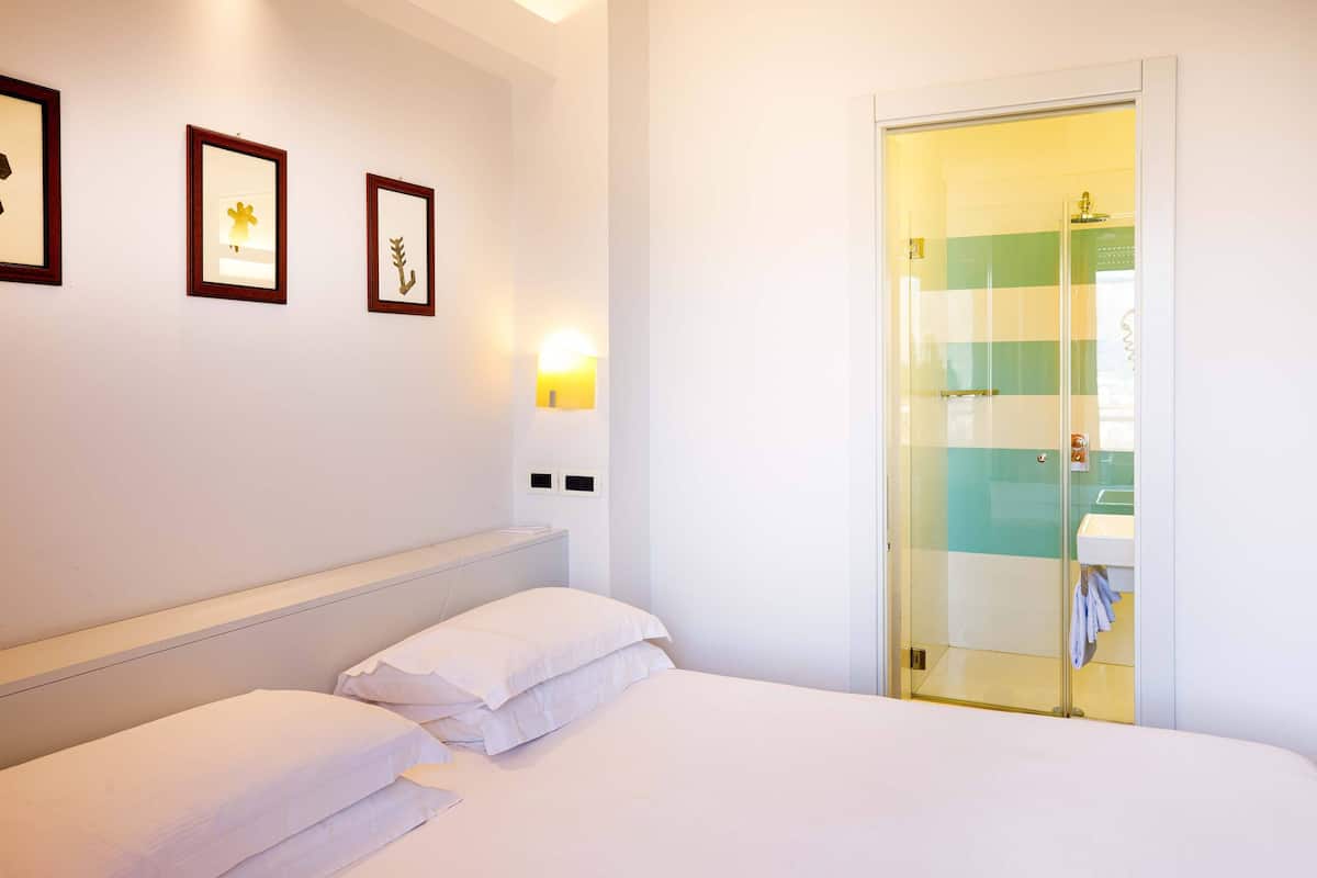 Ein Hotelzimmer mit einem Bett, einem Nachttisch, einem Spiegel und einer Dusche mit Glastür.