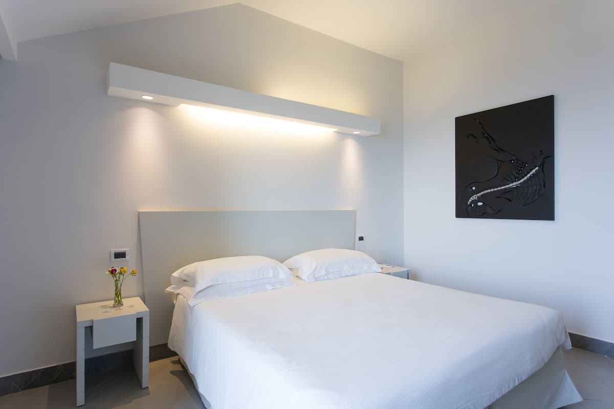 Ein modernes Schlafzimmer mit einem großen Bett, einem Nachttisch mit Blumenvase, Wandkunst und einer Deckenleuchte.