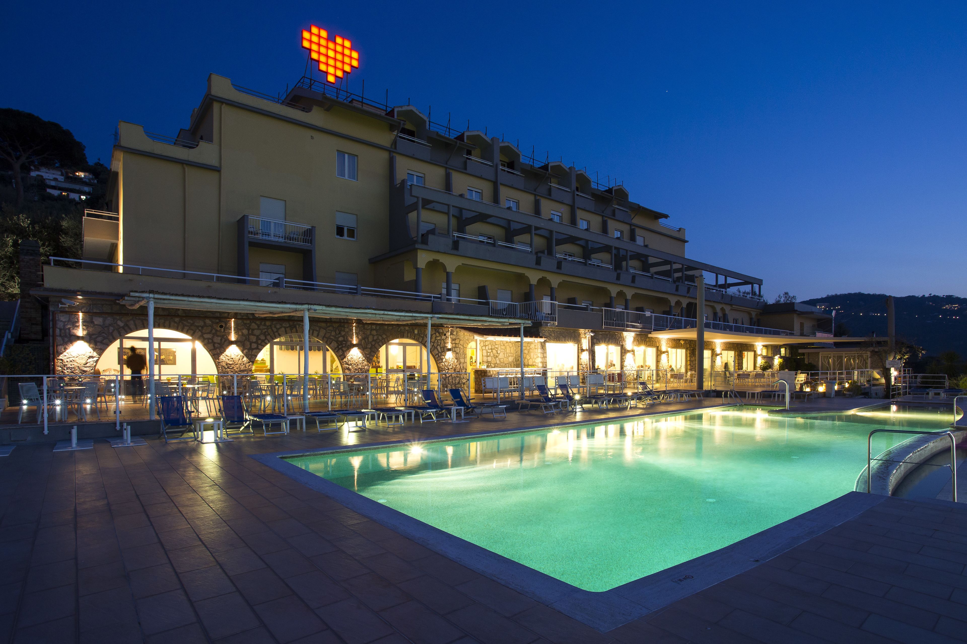 A hotel with a swimming pool, outdoor seating, and a large illuminated sign on the roof.
