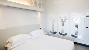 Un dormitorio moderno con una cama grande, ropa de cama blanca, un cabecero y una obra de arte colgada en la pared.