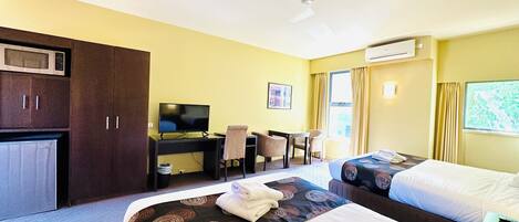 Quarto de hotel com duas camas, uma escrivaninha, uma televisão, uma cadeira e uma janela com cortinas.