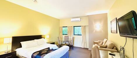 A hotel room with a bed, bedside tables, a desk with a chair, a TV, and a window with curtains.