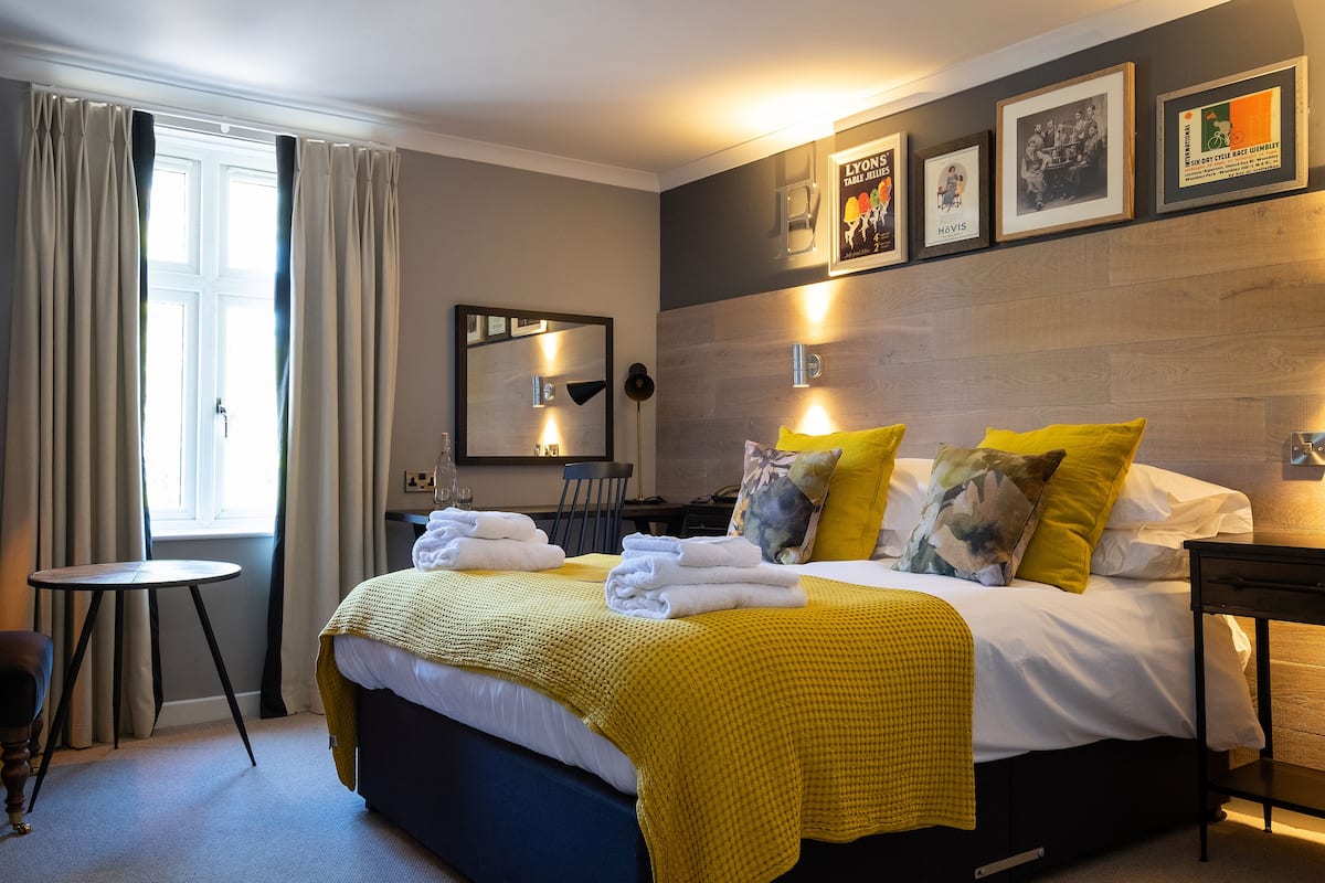 A hotel room with a bed, a small table, a chair, and a window with curtains.