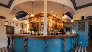 A bar area with a checkered floor, wooden bar counter, and hanging lights. - The Bridge Hotel Greenford (Greenford)