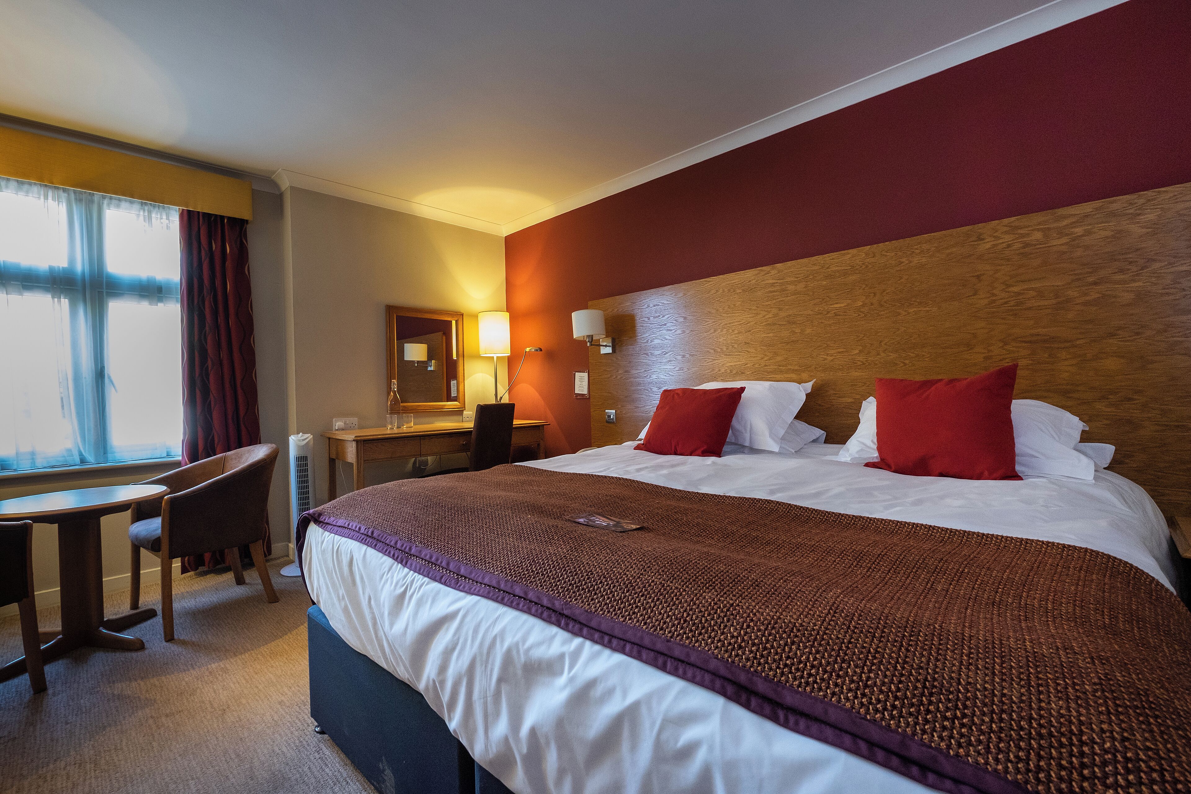 Ein Hotelzimmer mit einem großen Bett, einem Schreibtisch, einem Stuhl und einem Fenster mit Vorhängen.