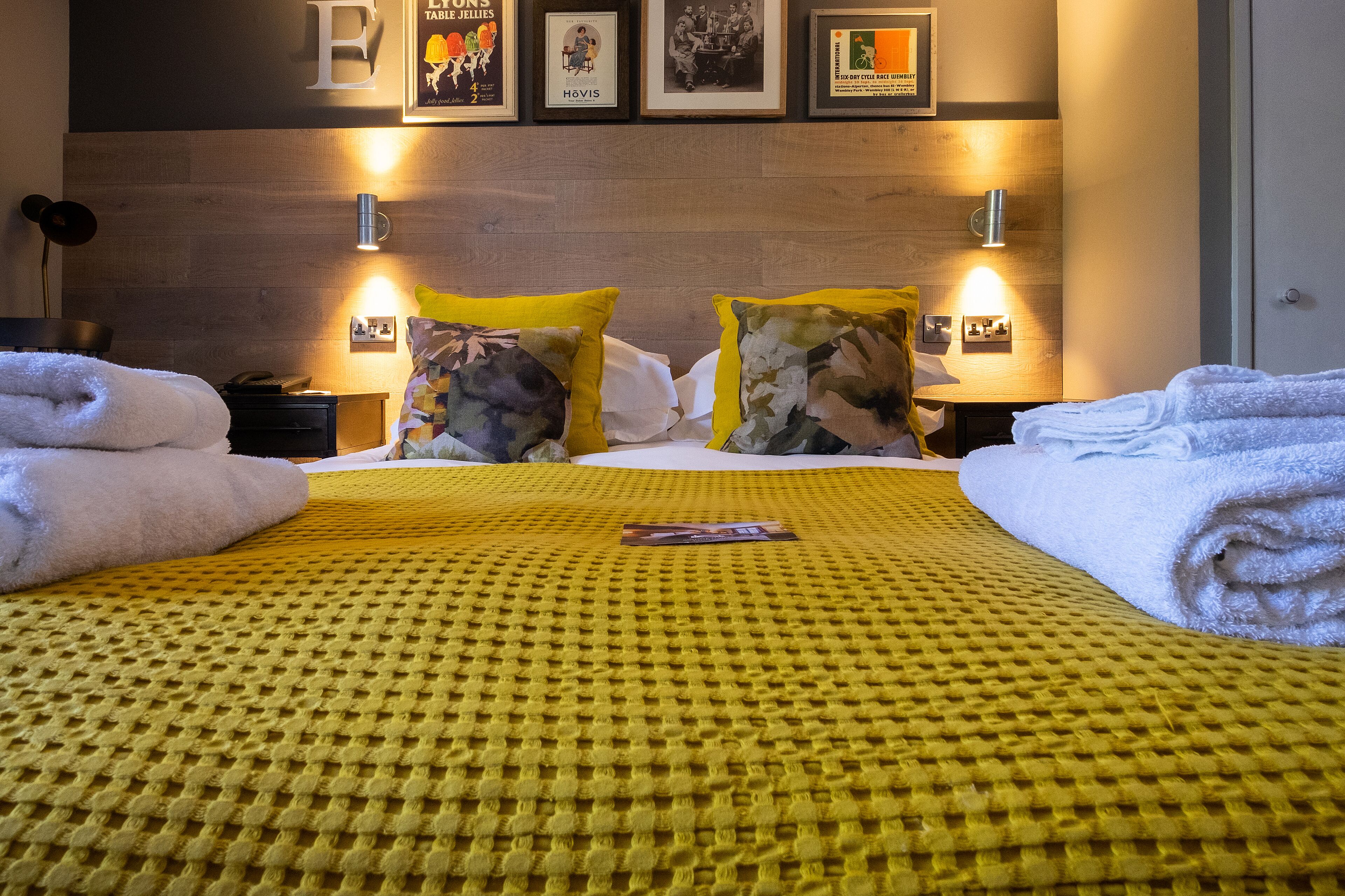 A neatly made bed with yellow and white bedding, two pillows, and a folded towel on each side.