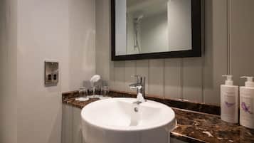 A bathroom with a white sink, a mirror, and a shower. There are two bottles of Green & Spring body lotion on the counter.