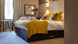 A neatly made bed with a yellow blanket, a bedside table with a lamp, and a large mirror on the wall. - The Bridge Hotel Greenford (Greenford)
