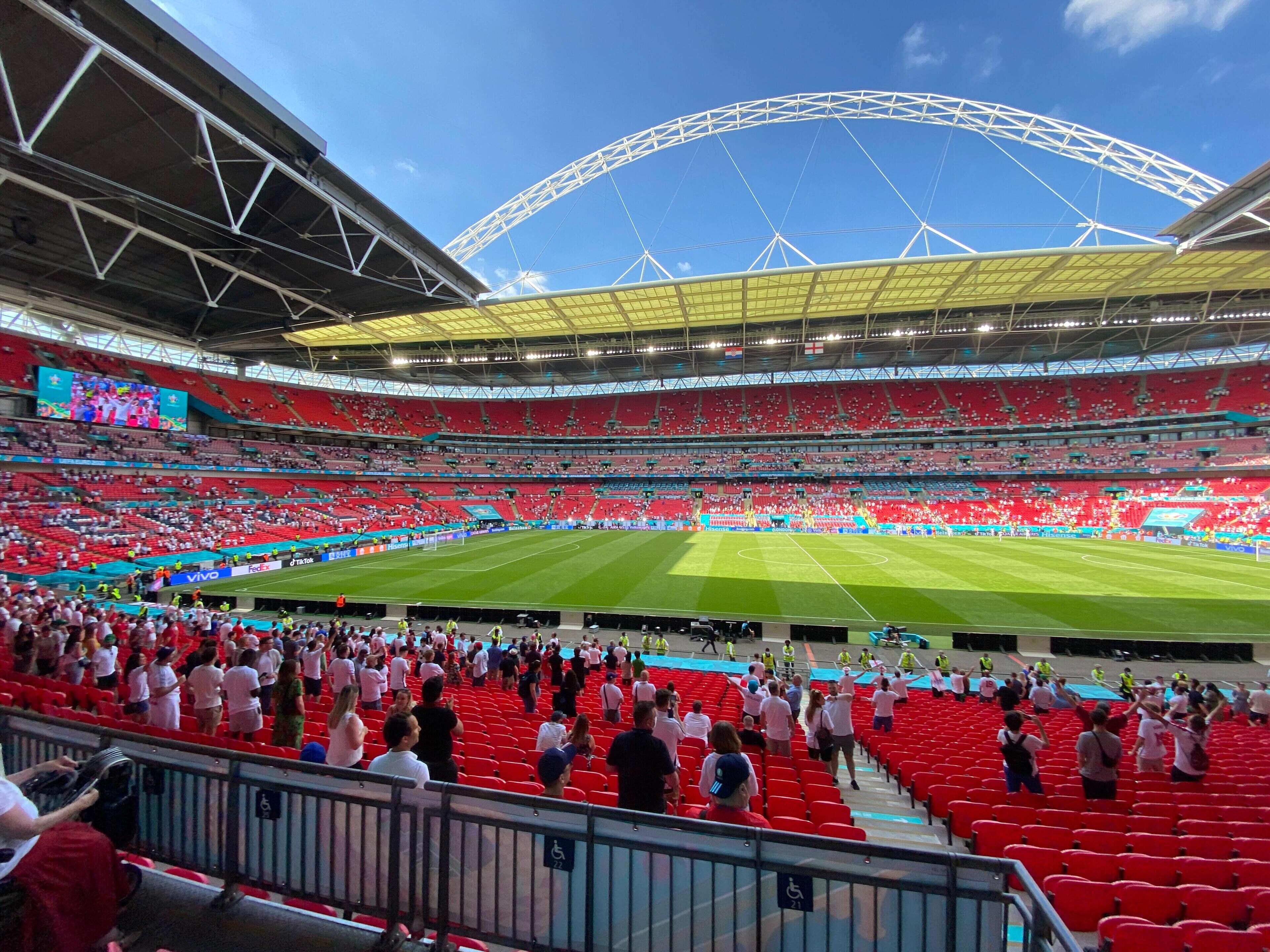 A stadium with multiple tiers of seating, a large central field, and a prominent arch structure in the background.