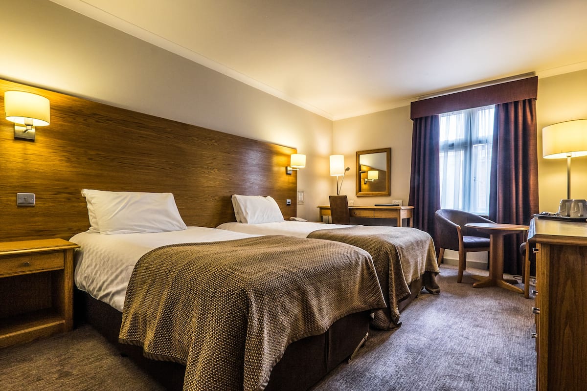 A hotel room with two beds, a desk, a chair, and a mirror.