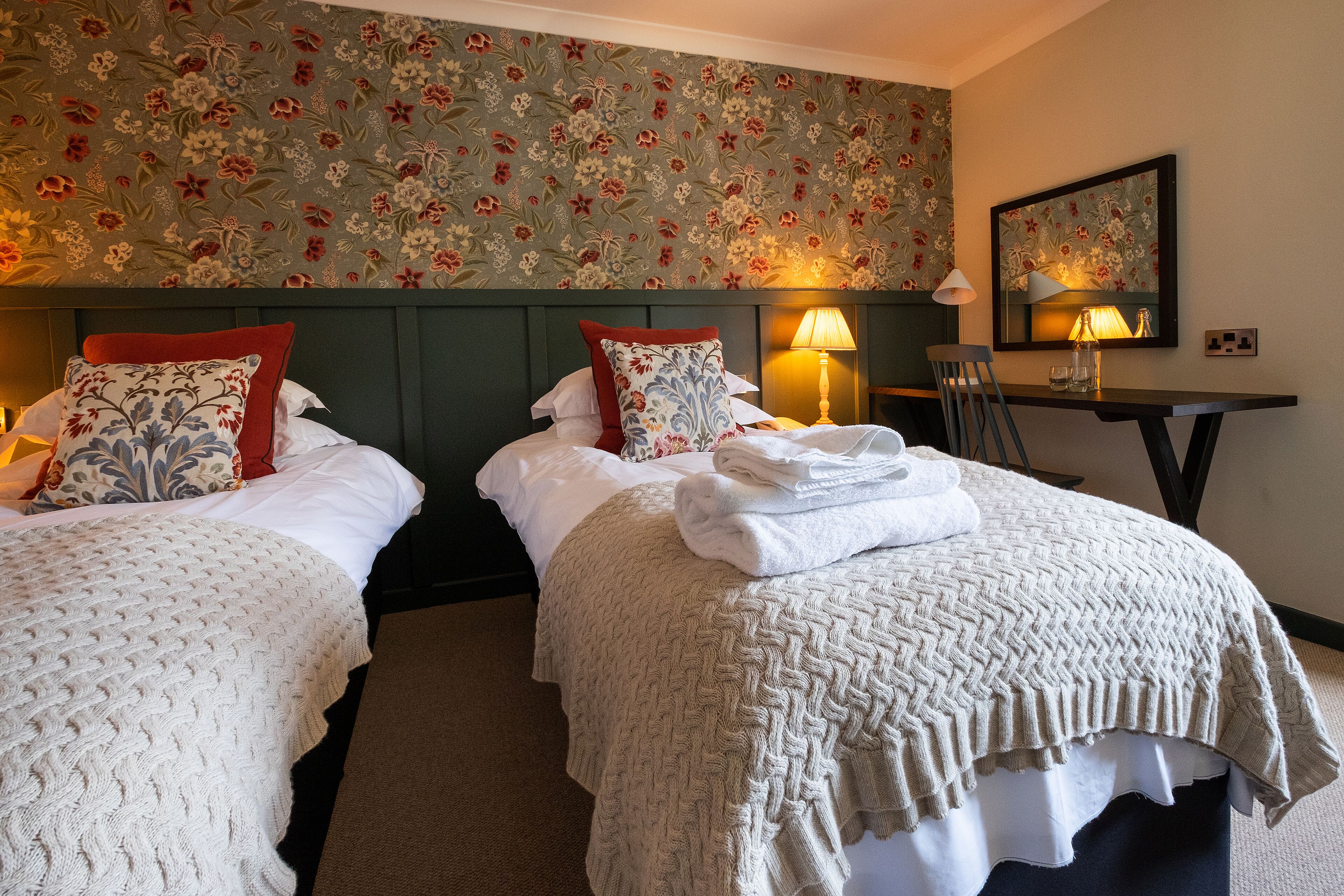 A hotel room with two beds, a desk, and a mirror.
