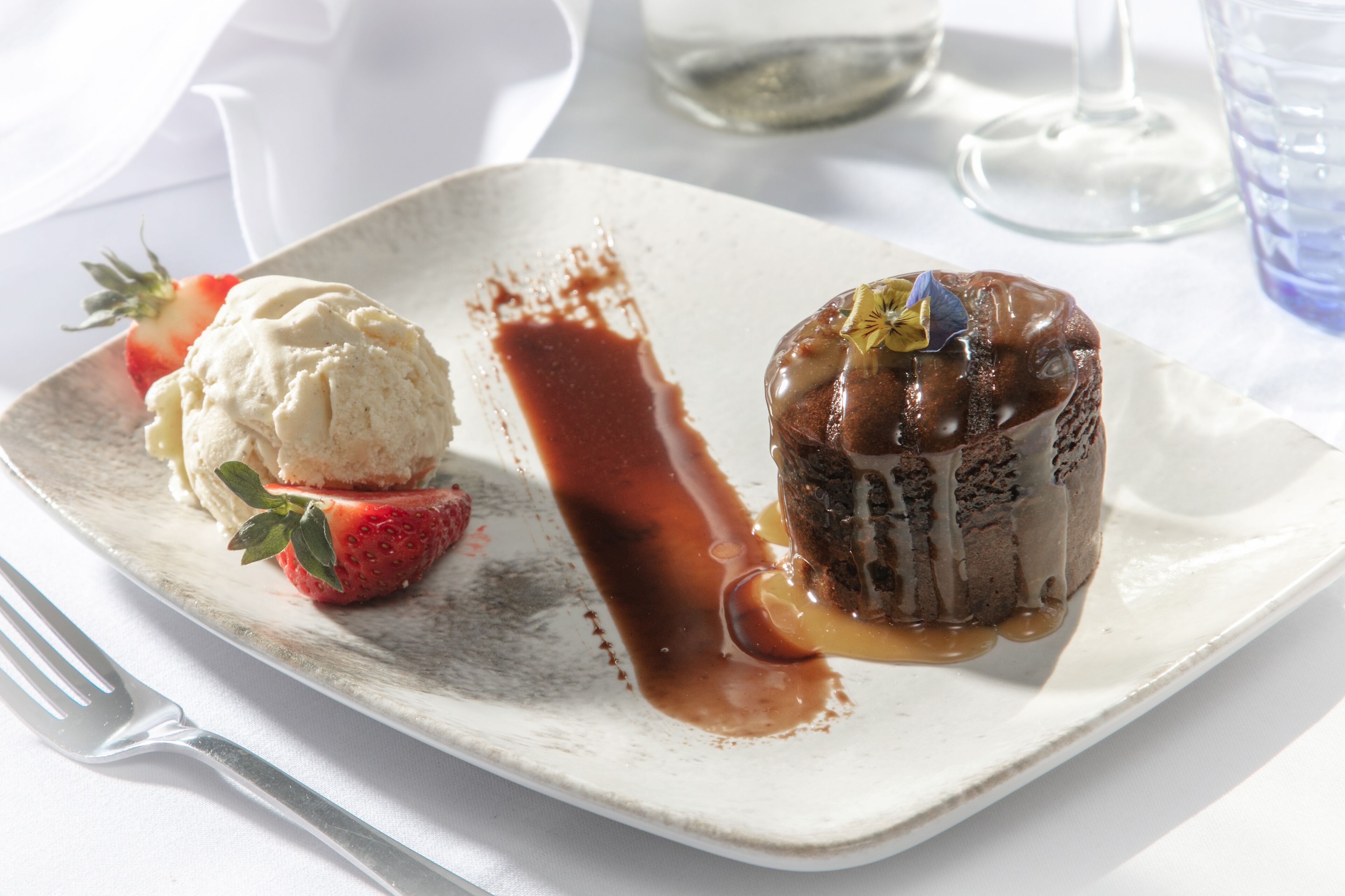 A dessert plate with a chocolate lava cake, a scoop of vanilla ice cream, and a strawberry.