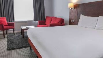 A hotel room with a large bed, a red sofa, a small table, and a lamp.