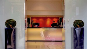 A reception area with a glass door, a reception desk, and two potted plants. - The Stuart Hotel Derby, Derby City Centre, Sure Collection by Best Western (Derby)