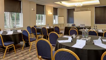 Uma sala de conferência com mesas redondas, cadeiras, cartões de nome, garrafas de água e uma tela de projetor.