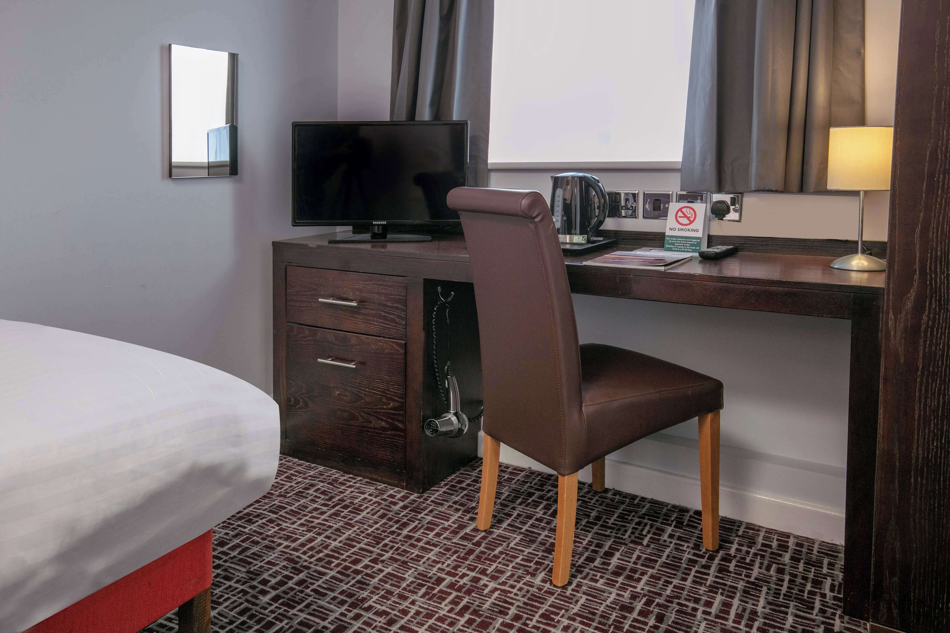 Une chambre d’hôtel équipée d’un lit, d’un bureau avec une télévision, d’une chaise, d’une machine à café et d’un panneau indiquant « Il est interdit de fumer ».