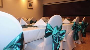 Sala de conferências com mesas redondas, toalhas brancas e cadeiras adornadas com fitas azuis-turquesa.