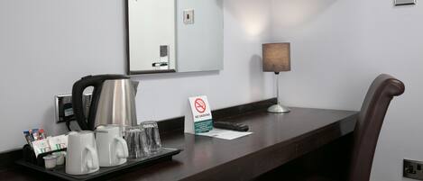A hotel reception desk with a coffee station, a no-smoking sign, a mirror, a television, and a lamp.