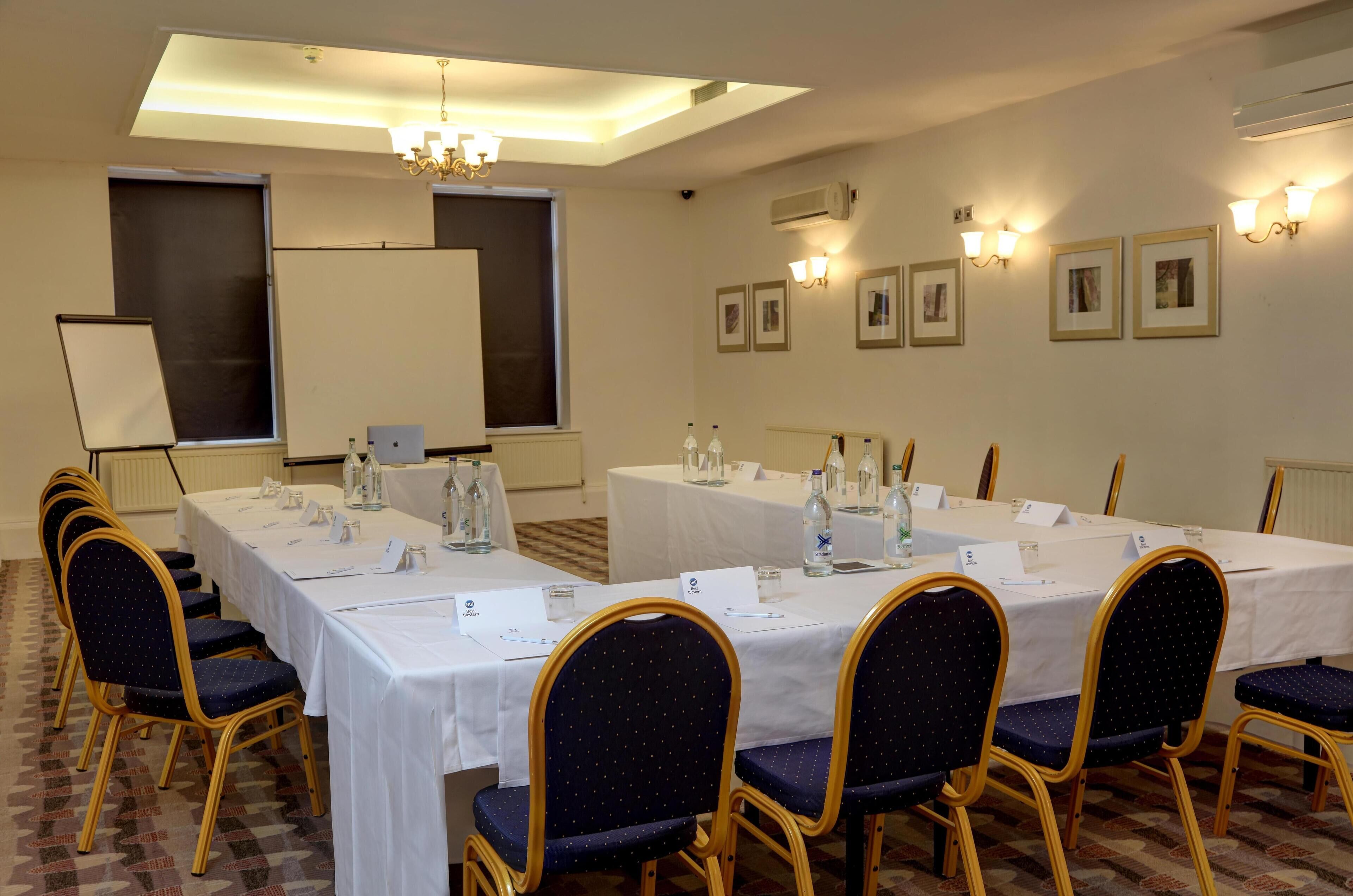 Une salle de conférence avec de longues tables, des chaises, des plaques nominatives et des bouteilles d’eau.