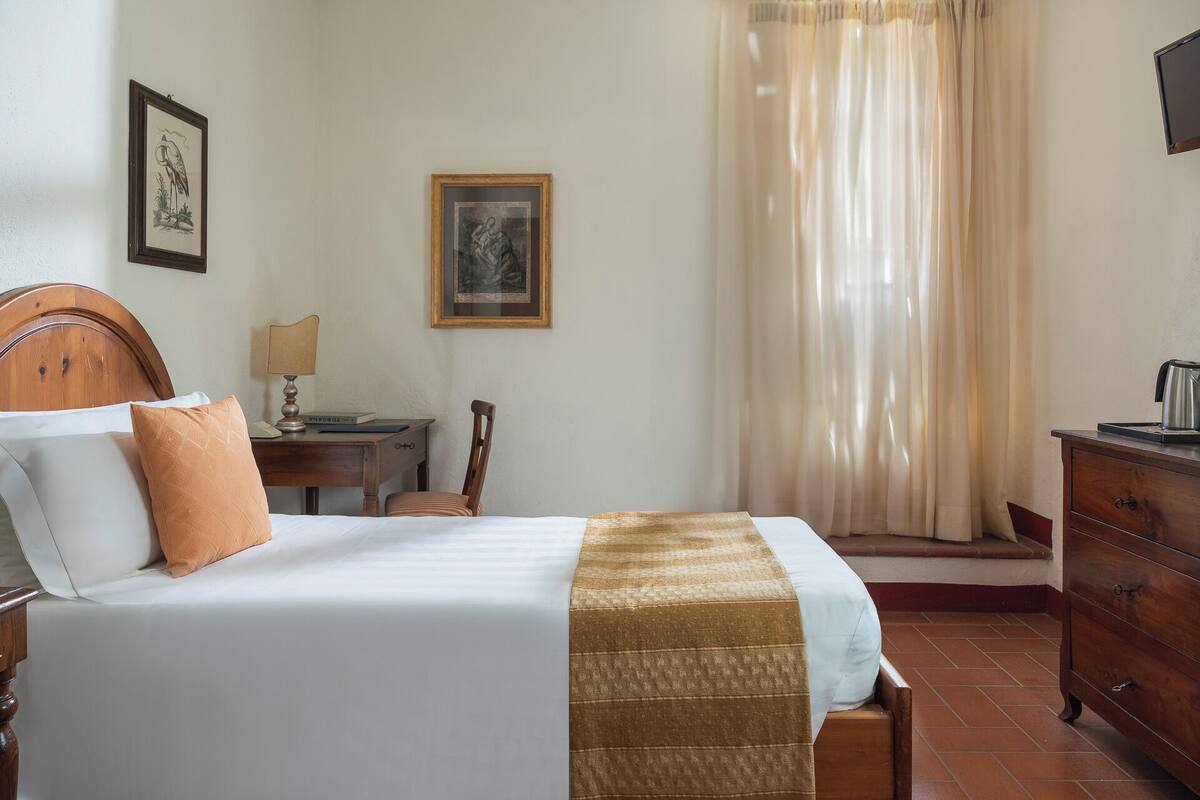 A neatly made bed with a wooden headboard, a bedside table with a lamp, a chair, and a dresser.