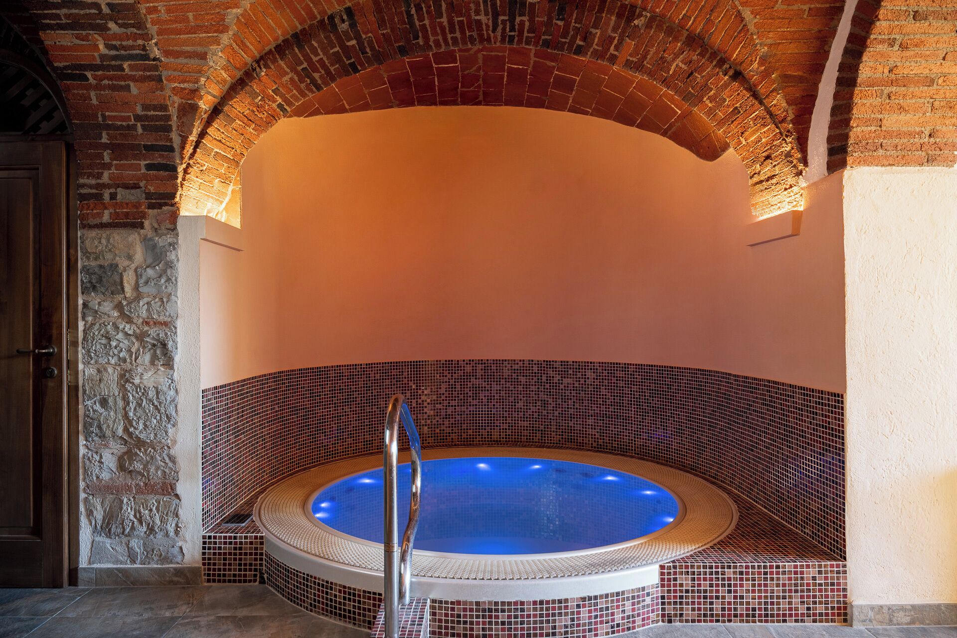 A spa area with a circular hot tub, stone walls, and a wooden door.