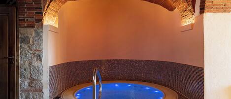A spa area with a circular hot tub, stone walls, and a wooden door.