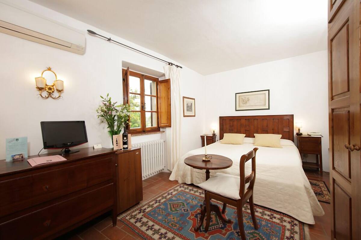 A bedroom with a bed, bedside table, lamp, TV, dresser, and a window with curtains.