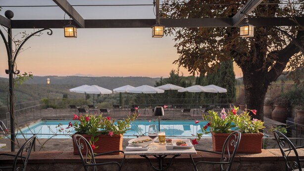 Un área de comedor al aire libre con piscina, plantas en macetas y sombrillas.