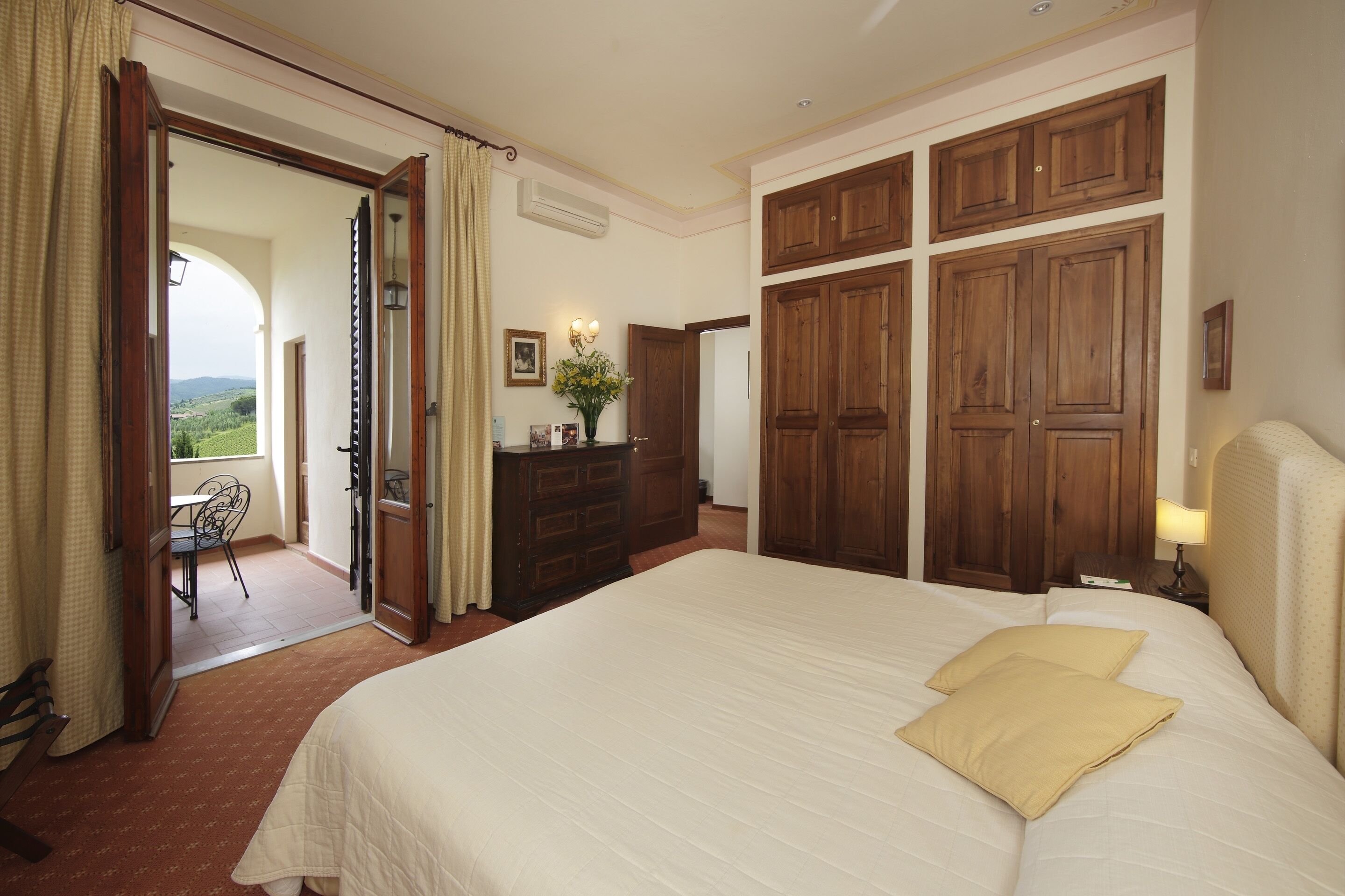 A hotel room with a large bed, wooden wardrobe, and a view of the outdoors.