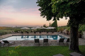 A poolside area with lounge chairs and umbrellas, surrounded by greenery and hills in the background.