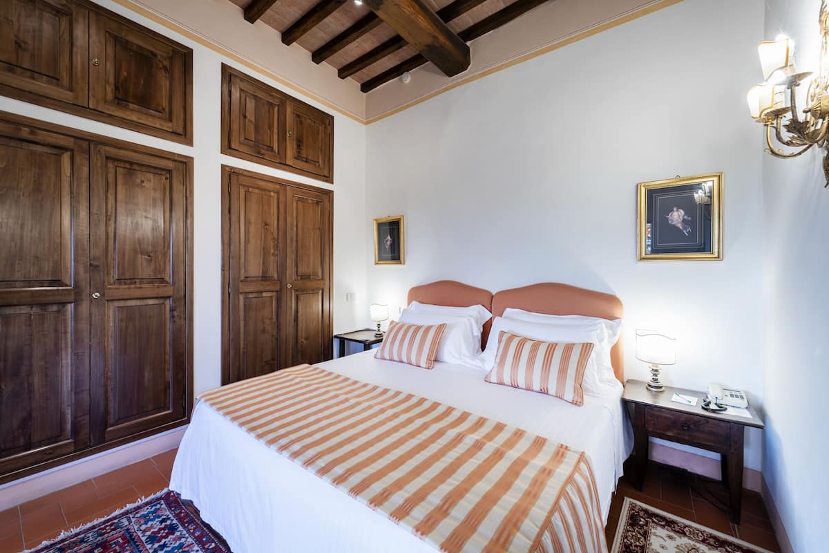A bedroom with a large bed, wooden wardrobe, and a nightstand with a lamp.