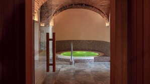 Zona de spa con un arco de ladrillo que conduce a una bañera de hidromasaje circular rodeada de mosaicos.
