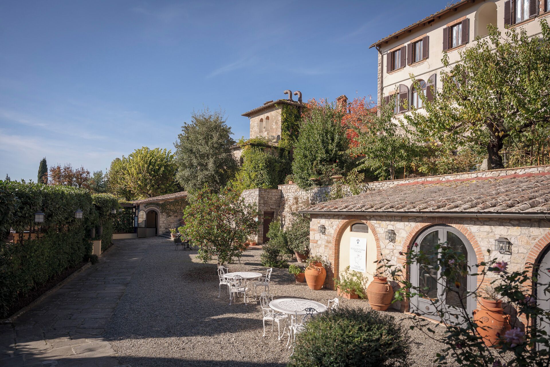 A courtyard with stone pathways, outdoor seating, and a building with arched windows and a tiled roof.