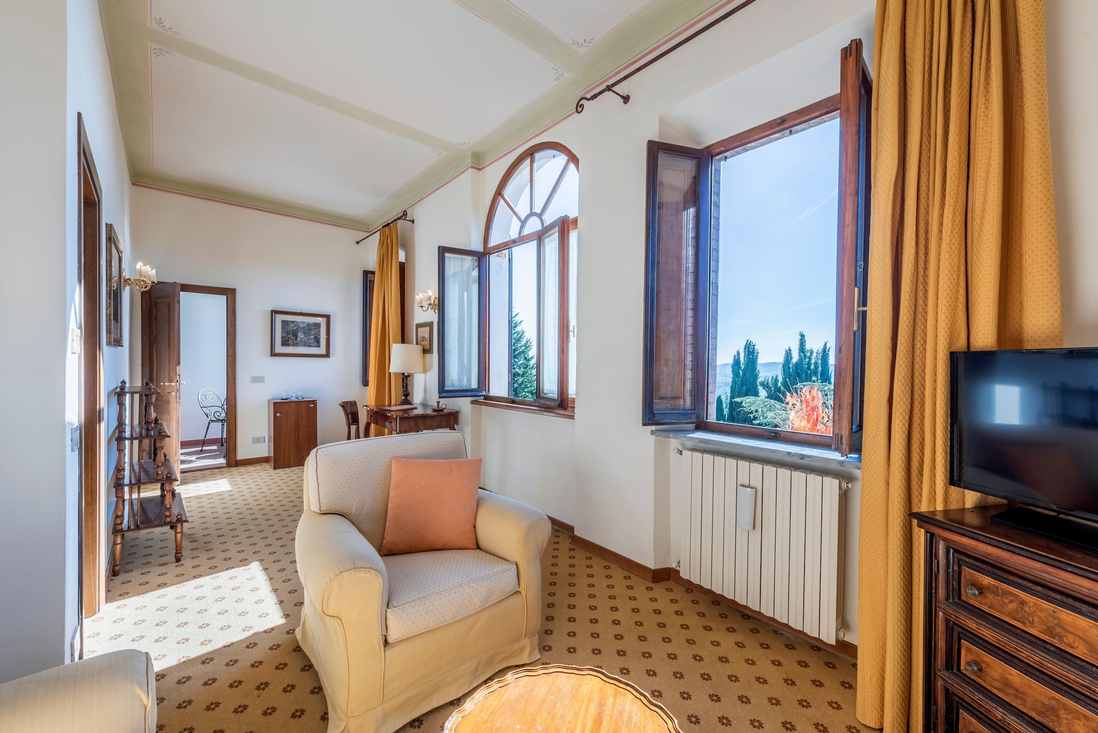 Un salón con sofá, televisor y ventanas amplias que dan a un paisaje de árboles.