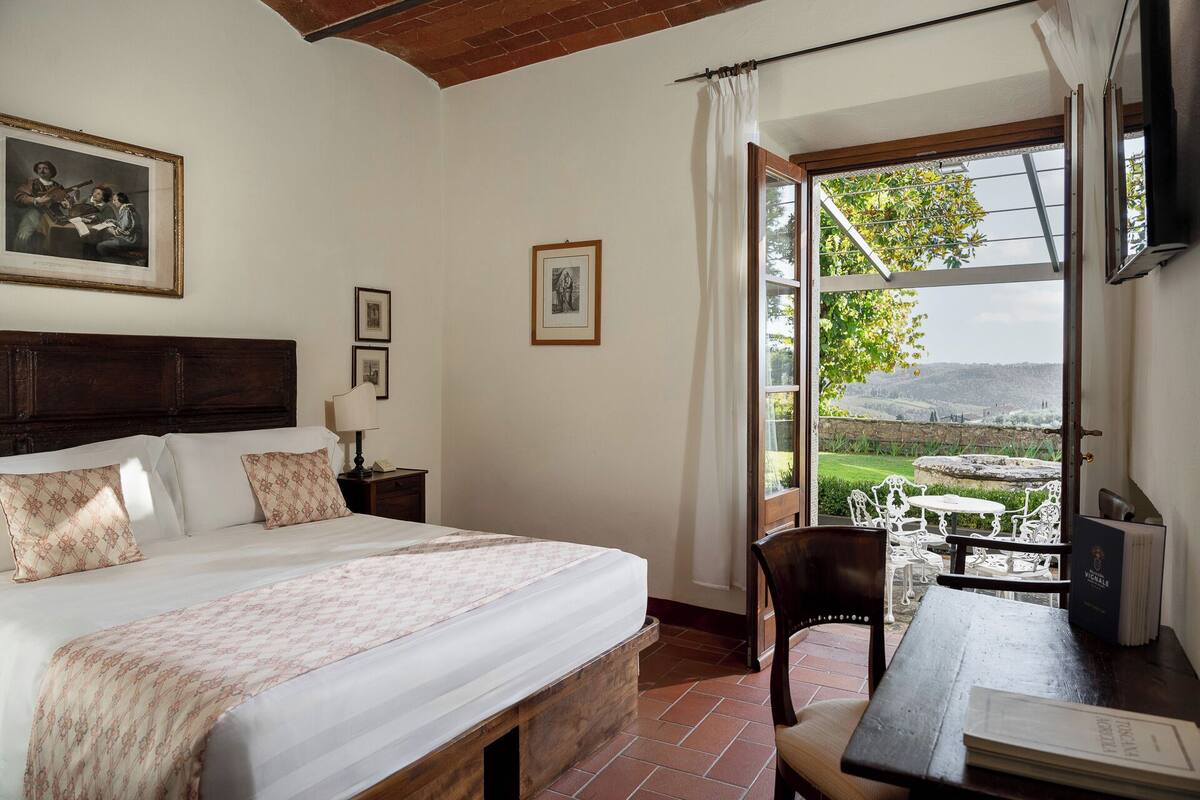 A bedroom with a bed, a desk, and a view of the outdoors.