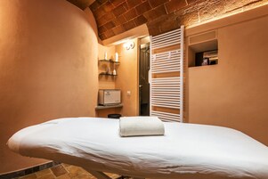 Un cuarto de spa con una camilla de masaje, una toalla, un estante con artículos de aseo y una zona de ducha.