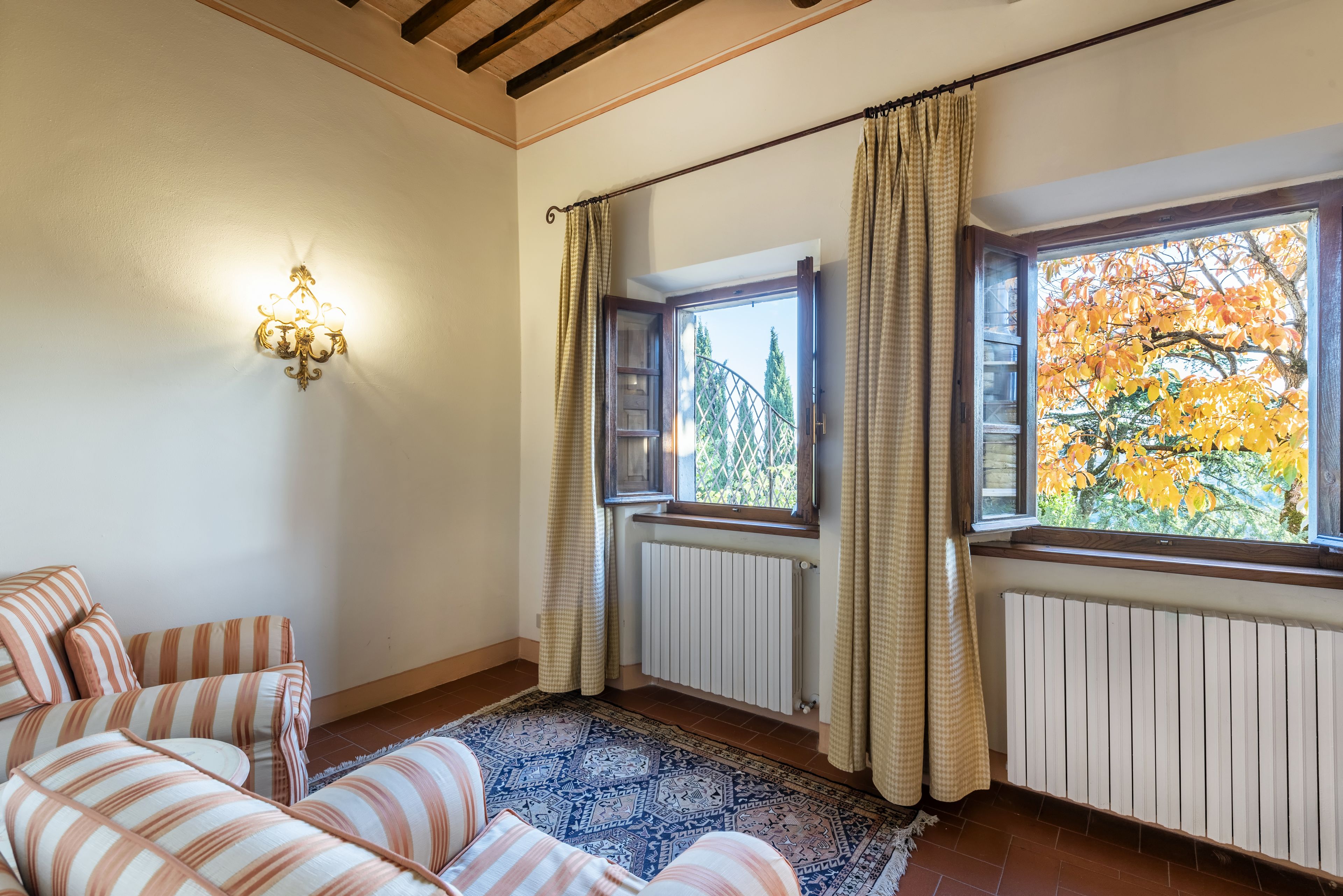 A room with striped sofas, a patterned rug, a wall-mounted light fixture, and a window with curtains.