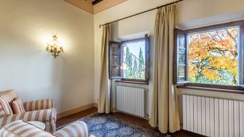 A room with striped sofas, a patterned rug, a wall-mounted light fixture, and a window with curtains.