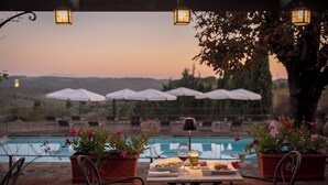 Un área de comedor al aire libre con una mesa dispuesta para dos, con vistas a una piscina y un viñedo.