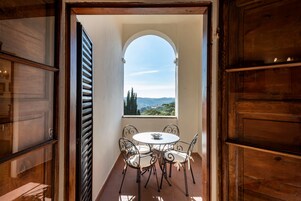 Una habitación con una mesa redonda y sillas, una ventana con vistas a árboles y colinas, y paneles de madera.