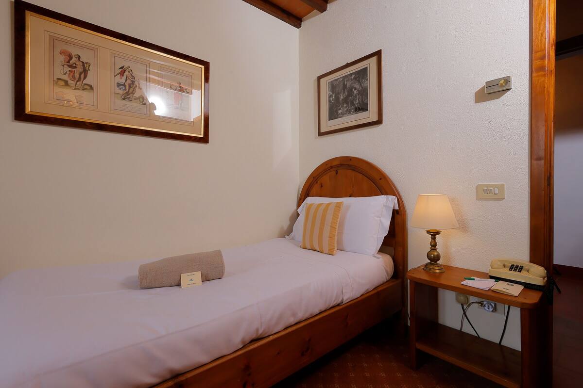 A single bed with a wooden headboard, a bedside table with a lamp, and framed pictures on the wall.