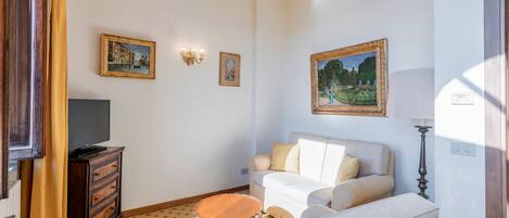 A living room with a television on a wooden cabinet, a white sofa, a patterned rug, and two framed paintings on the wall.