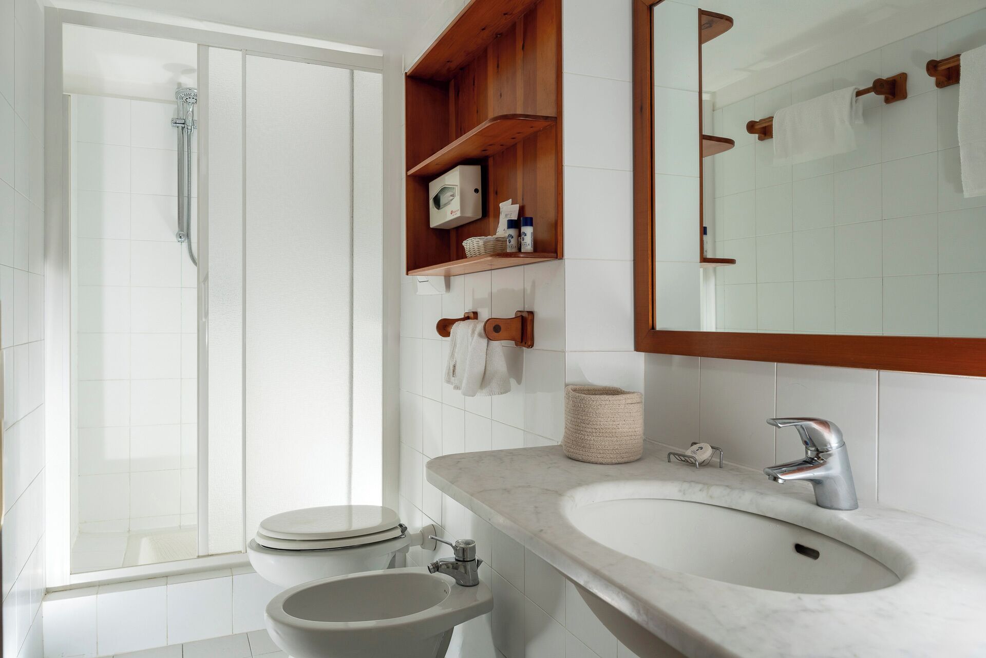 A modern bathroom with a shower, toilet, sink, and a wooden shelf with toiletries.