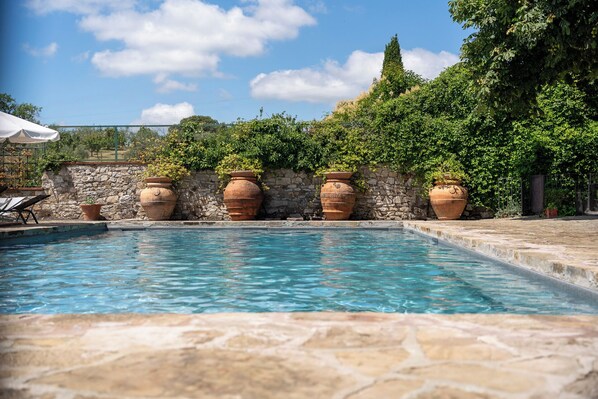A swimming pool with terracotta pots and a stone wall.