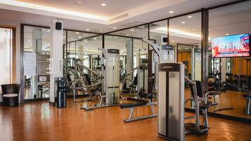 A gym with various exercise machines, a television screen, and a wooden floor.