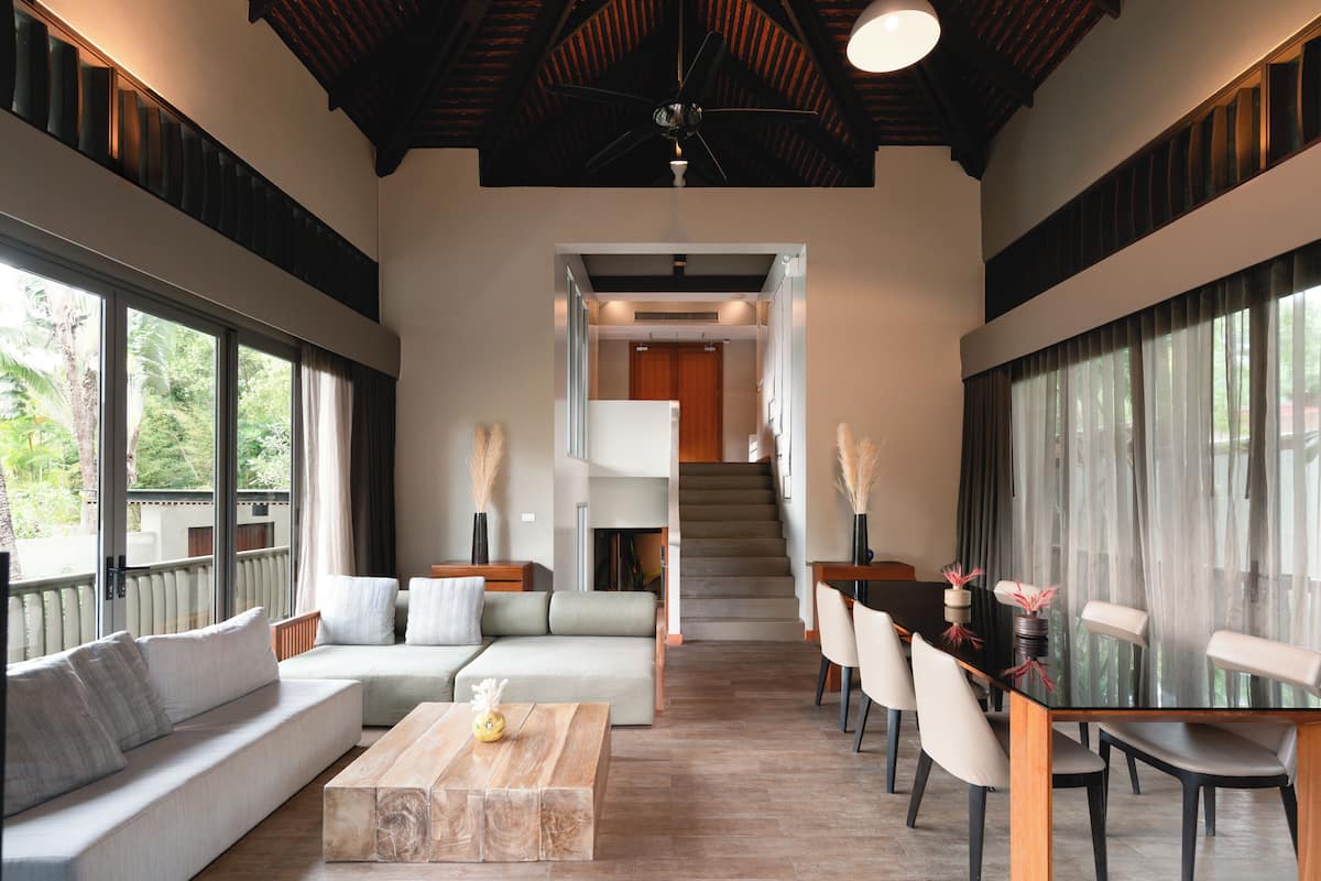 A spacious living area with a sofa, coffee table, and dining table with chairs. A staircase leads to an upper level.
