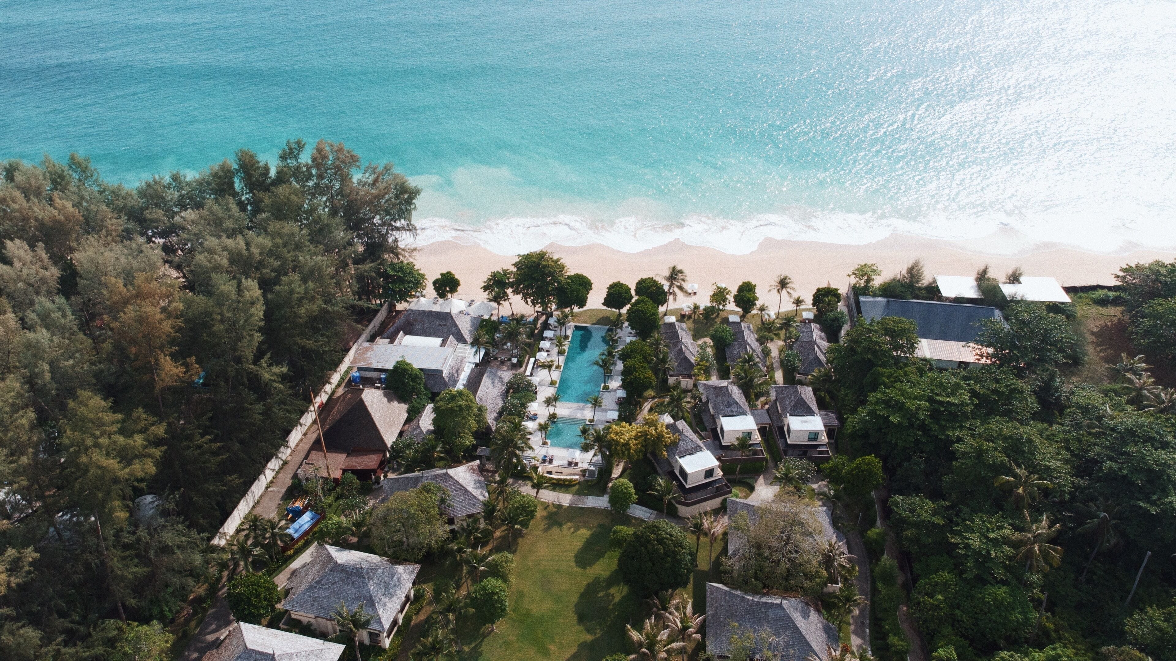 An aerial view of a resort with a swimming pool, beach, and lush greenery.