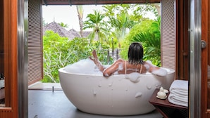 A person relaxing in a large bathtub with a view of lush greenery and a traditional roof structure in the background. - Layana Resort and Spa - Adult Only (Ko Lanta)